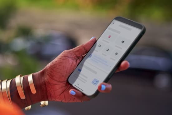 Against a blurry background, a woman's hand with blue nail polish and gold bracelets holds a smartphone open to the Uber app's safety features.